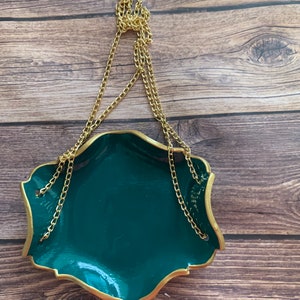 Op de afbeelding: Een donkergroene hangende schaal met een gouden rand en een gouden ketting. De schaal hangt aan een gouden ring.