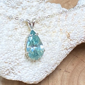 Puede incluir: Un collar de cadena de plata con un colgante de piedra preciosa azul claro en forma de pera.
