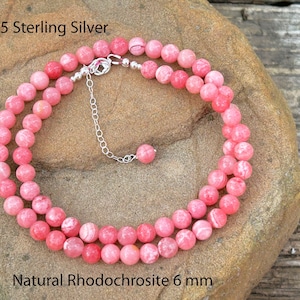 May include: A necklace made of pink rhodochrosite beads, each 6 mm in diameter, strung on a silver chain. The necklace is .925 sterling silver. The beads are a mix of light and dark pink.