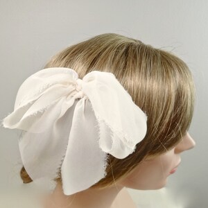 May include: A white chiffon bow hair clip. The bow is tied with a loose knot and has frayed edges.