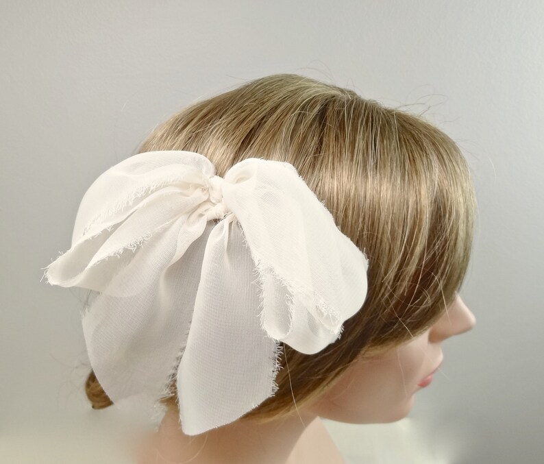 May include: A white chiffon bow hair clip. The bow is tied with a loose knot and has frayed edges.