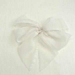 May include: A white silk ribbon bow with frayed edges. The bow is tied in a simple knot and is ready to be used for a variety of purposes.