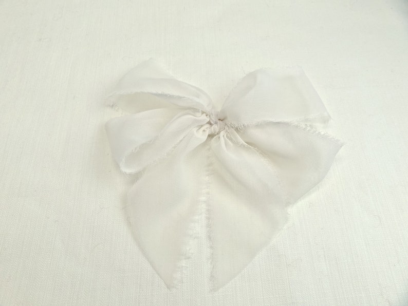 May include: A white silk ribbon bow with frayed edges. The bow is tied in a simple knot and is ready to be used for a variety of purposes.
