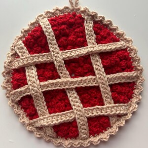 May include: A handmade crochet pie-shaped hot pad. The center is a vibrant red, resembling a pie filling, with a lattice crust in a light tan color. The edges are scalloped, and a loop is attached for hanging. A charming kitchen accessory.