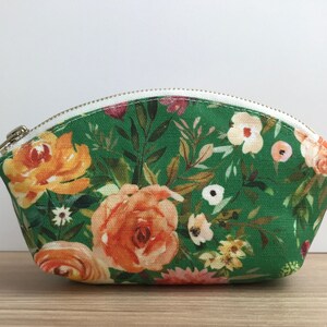 May include: A green zippered pouch with a floral print featuring orange, yellow, and white flowers. The pouch is made of fabric and has a white zipper.