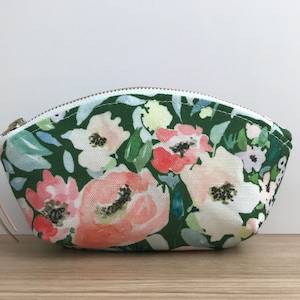 May include: A green and white floral print zippered pouch with a light brown zipper pull.