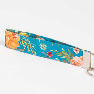 May include: A teal blue key chain with a floral pattern featuring orange, yellow, pink, and red flowers. The key chain has a silver metal ring and a silver metal clasp.