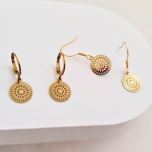May include: A set of three gold-toned earrings with a delicate, circular design. The earrings feature a mandala-like pattern with intricate details.