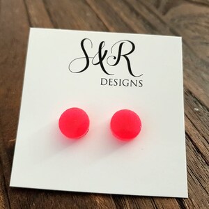 May include: A pair of bright pink round stud earrings on a white card with the text "S&R Designs".