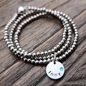 May include: A silver beaded bracelet with a charm that says "IMMY" and has a small blue gemstone.