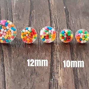 May include: A set of six colourful sprinkle-filled resin earrings in various sizes, ranging from 8mm to 15mm. The earrings are displayed on a wooden surface.