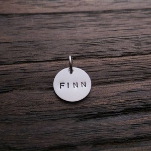 May include: A silver round tag with the name "FINN" engraved on it.