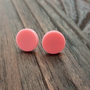 May include: A pair of pink round stud earrings. The earrings are made of a smooth, matte material and are a light shade of pink.