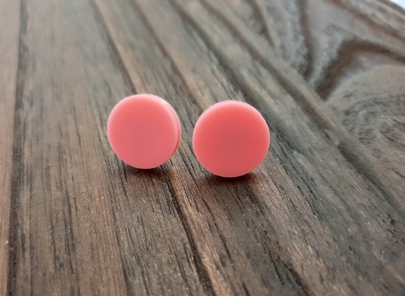 May include: A pair of pink round stud earrings. The earrings are made of a smooth, matte material and are a light shade of pink.