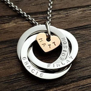 May include: A silver-toned necklace featuring three interlocking circular rings and a small rose gold-toned heart charm. The rings are engraved with the names Gracie, Finlay, and Edison, while the heart charm is engraved with the name Matt.