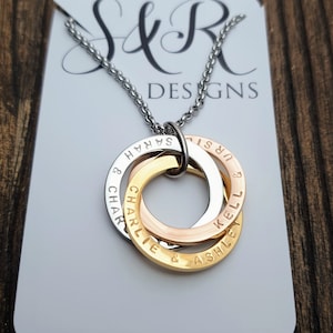 May include: A silver chain necklace with three interlocking rings. The rings are engraved with the names "Sarah & Charlie", "Kell & Ashley", and "Jur & Sarah".