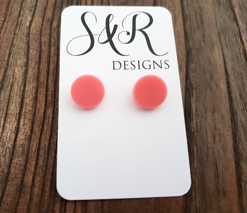 May include: A pair of pink round stud earrings on a white card with the text "S&R Designs".