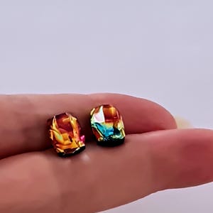 May include: A pair of iridescent earrings with a faceted, geometric design. The earrings are a mix of orange, red, green, and blue.