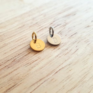May include: Two small round metal charms with a letter 'B' engraved on them. One charm is gold and the other is silver.