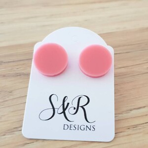 May include: A pair of pink round stud earrings on a white card with the text "S&R DESIGNS".