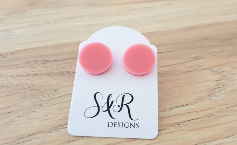 May include: A pair of pink round stud earrings on a white card with the text "S&R DESIGNS".