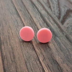 May include: A pair of pink round stud earrings. The earrings are made of a smooth, matte material.