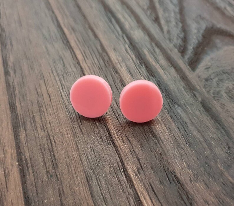 May include: A pair of pink round stud earrings. The earrings are made of a smooth, matte material.