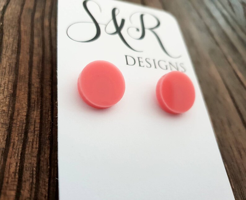 May include: A pair of pink round stud earrings on a white card with the text "S&R Designs".