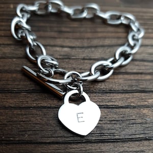 以下が含まれることがあります： ハート型のチャームに「E」の文字が刻まれたシルバーチェーンブレスレットです。