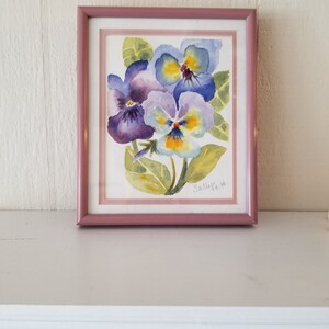 May include: A framed watercolour painting of purple and yellow pansies with green leaves. The painting is signed "Sally Ya 96".