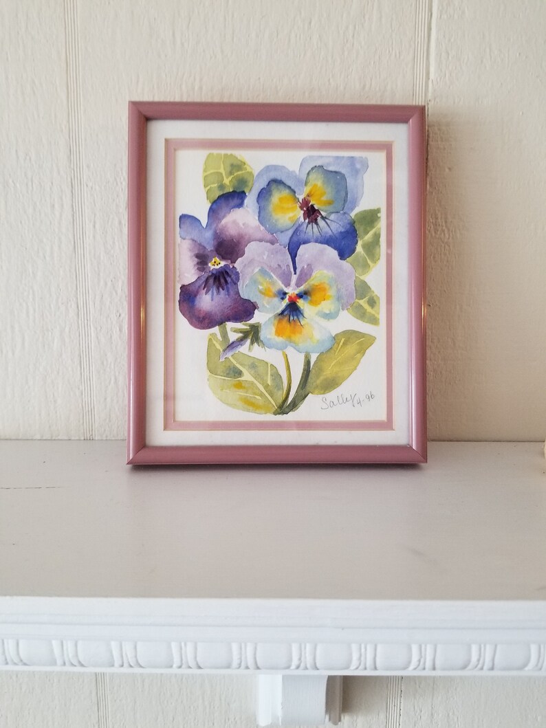May include: A framed watercolour painting of purple and yellow pansies with green leaves. The painting is signed "Sally Ya 96".