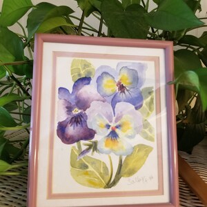 May include: A framed watercolour painting of purple and yellow pansies with green leaves. The painting is signed "Sallee '96".