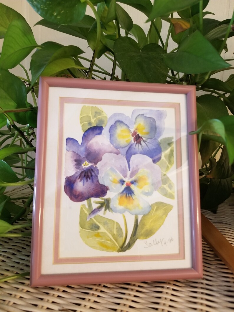 May include: A framed watercolour painting of purple and yellow pansies with green leaves. The painting is signed "Sallee '96".
