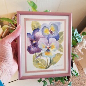 May include: A framed watercolour painting of three purple and yellow pansies with green leaves. The painting is signed "Sally '96".