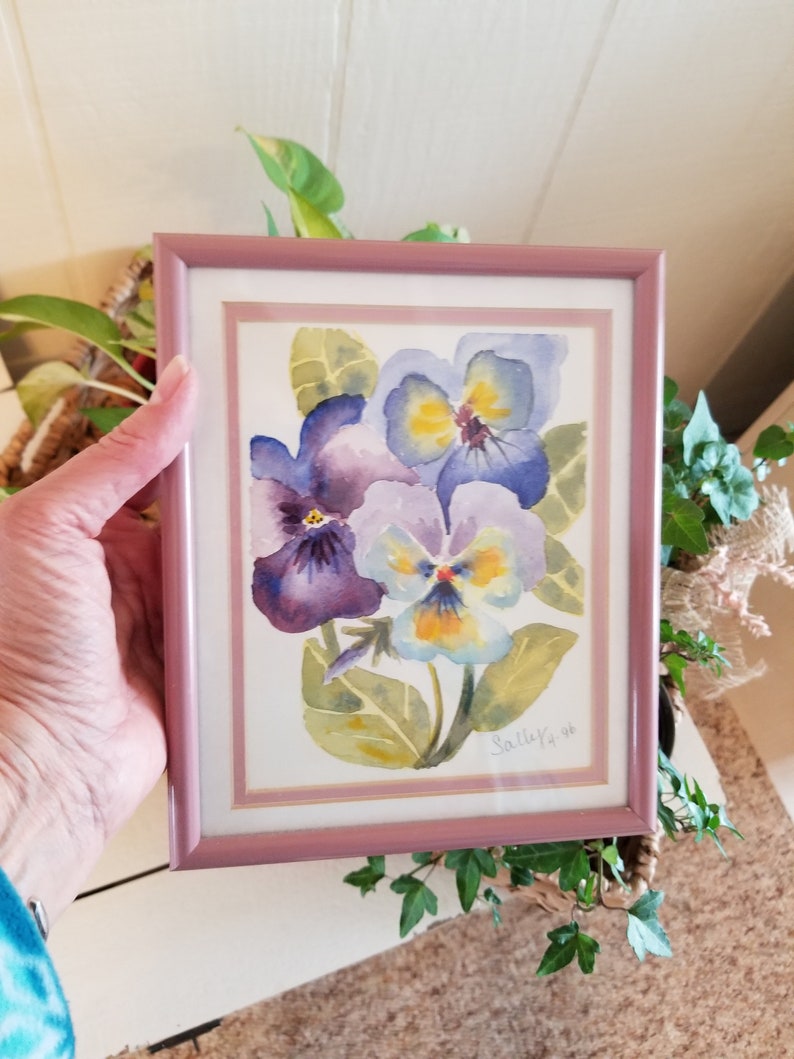May include: A framed watercolour painting of three purple and yellow pansies with green leaves. The painting is signed "Sally '96".