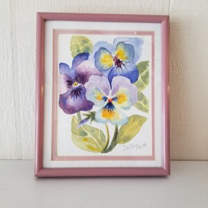 May include: A framed watercolour painting of three purple, blue, and yellow pansies with green leaves. The painting is signed "Sally K 96".