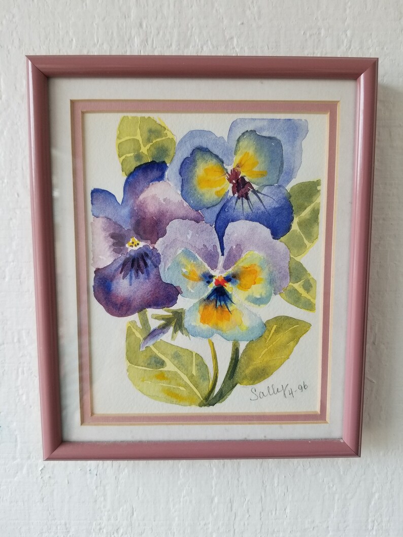 May include: A framed watercolour painting of three purple, blue, and yellow pansies with green leaves. The painting is signed "Sally '96".