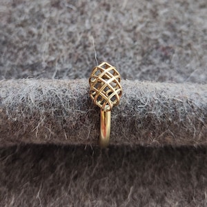 May include: A gold ring with a geometric, cage-like design. The ring is made of a single, continuous piece of metal.