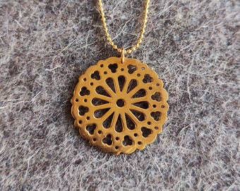 Könnte beinhalten: Eine goldene Halskette mit einem runden, filigranen, durchbrochenen Anhänger. Der Anhänger hat ein florales Design mit einem kreisförmigen Zentrum.