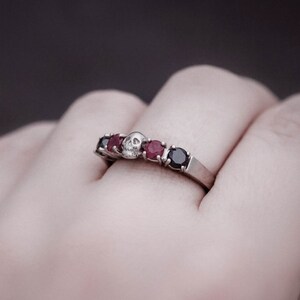 May include: A silver ring with a skull design and red and black gemstones.