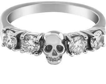 May include: A silver ring with a skull design and five clear round stones.