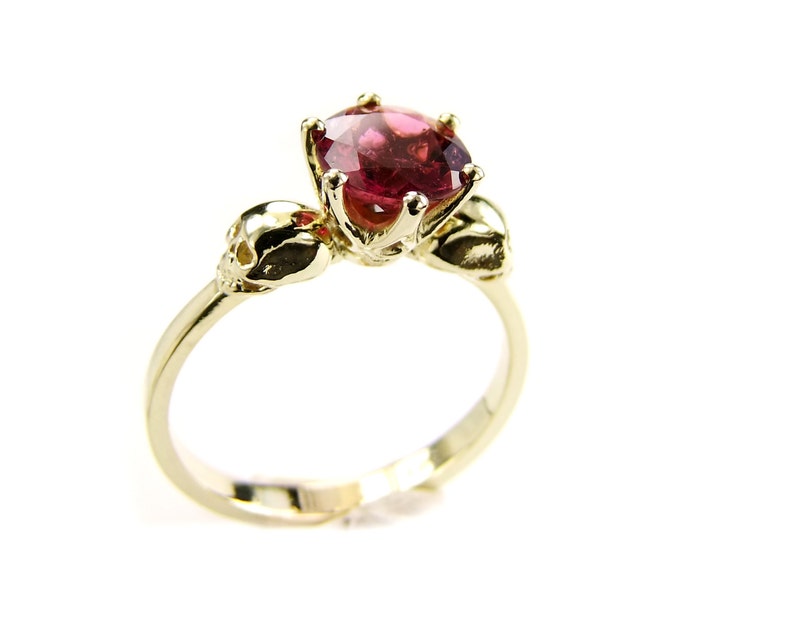 May include: A gold ring with a pink gemstone and two skull accents.