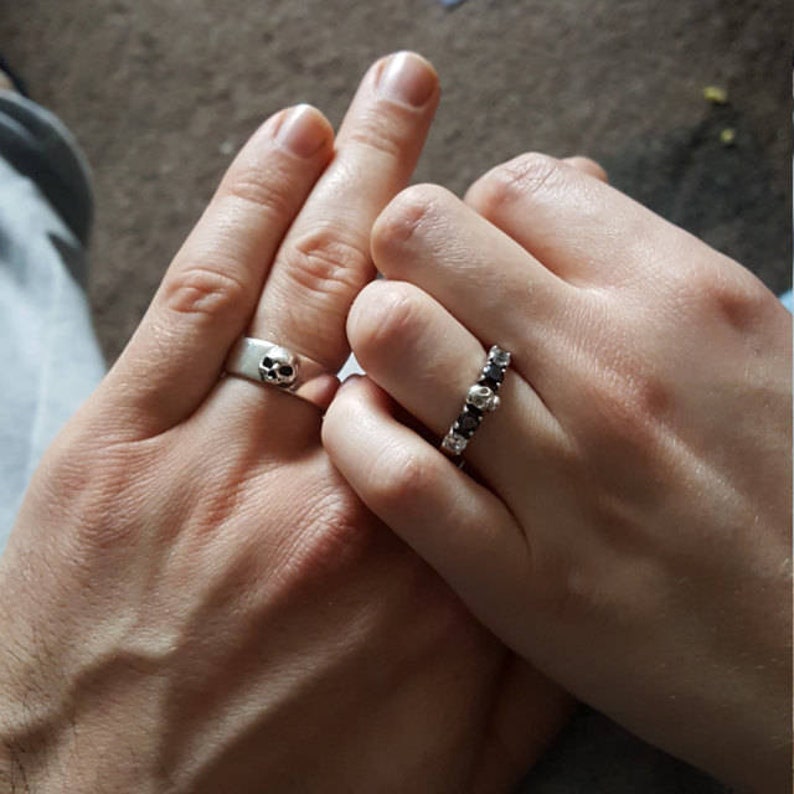 May include: Two silver rings with skull designs. One ring has a single skull, the other has a row of skulls.
