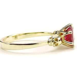 May include: A gold ring with a large red gemstone and two skull accents on the band.