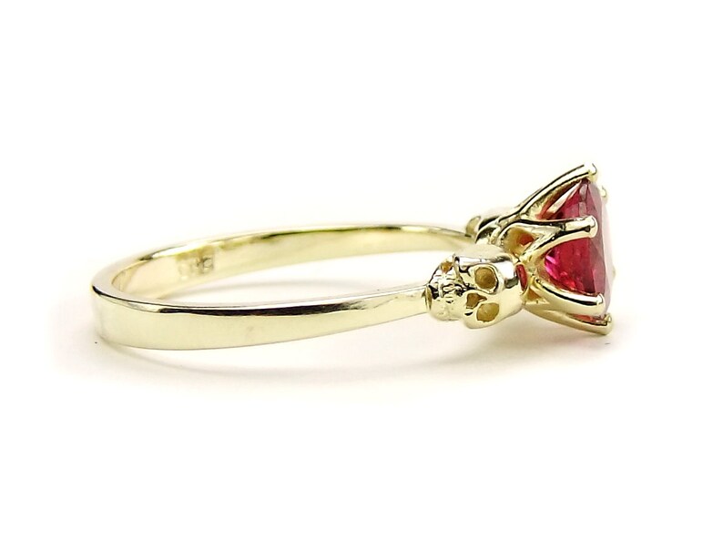 May include: A gold ring with a large red gemstone and two skull accents on the band.