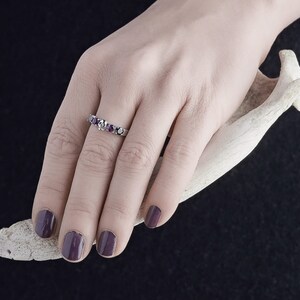 May include: A silver ring with a row of purple gemstones. The ring is on a person's finger.