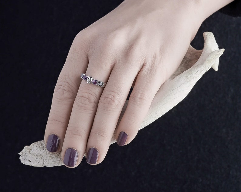 May include: A silver ring with a row of purple gemstones. The ring is on a person's finger.