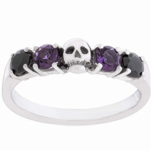 May include: A silver ring with a skull design and three gemstones. Two of the gemstones are purple and one is black.