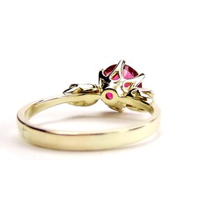 May include: A gold ring with a red gemstone set in a delicate, intricate design. The ring has a simple band and a detailed setting for the gemstone.