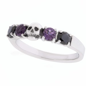 May include: A silver ring with a skull charm and black and purple gemstones.